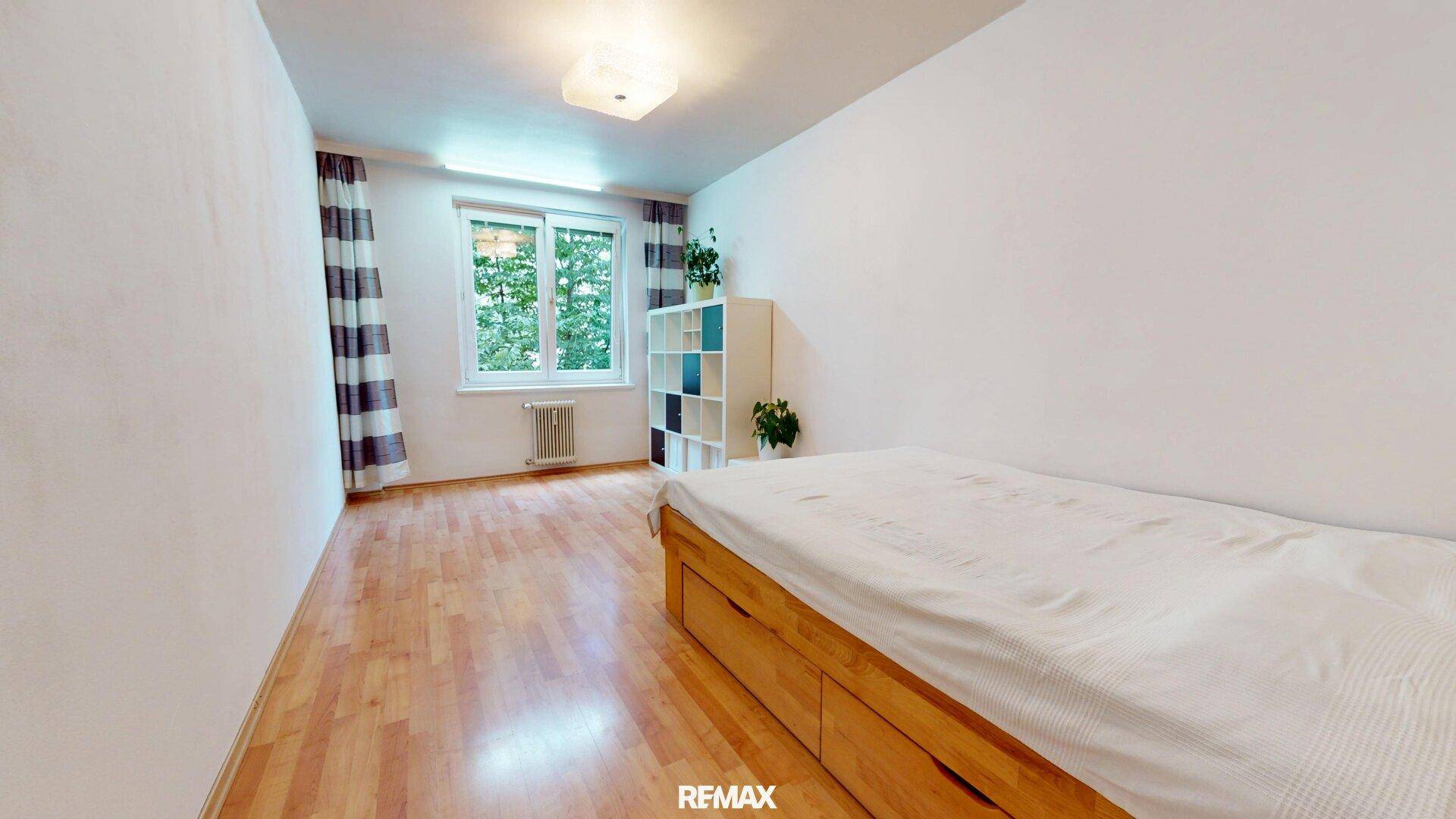Schlafzimmer mit Holzbett, Parkettboden und einem Fenster mit Blick ins Grüne.
