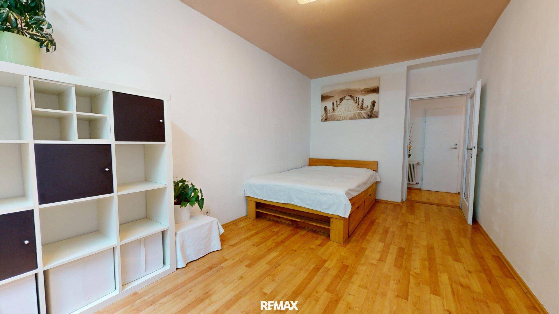 Schlafzimmer mit Holzbett, Parkettboden und einem praktischen Regalsystem.