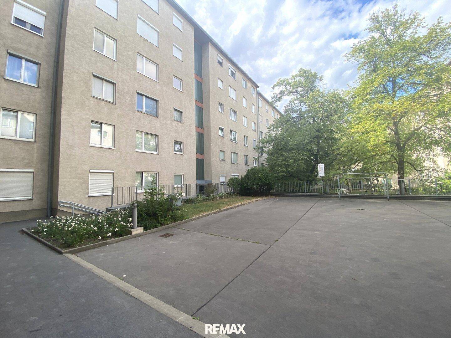 Außenansicht eines Wohngebäudes mit großem Parkplatz und viel Grünfläche.