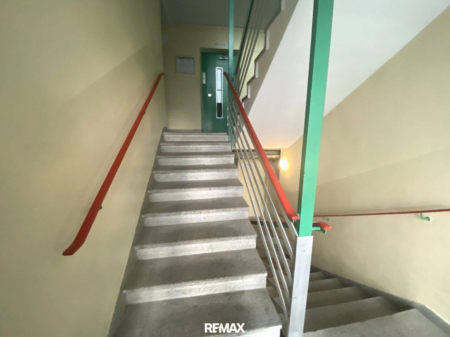 Treppenhaus eines Gebäudes mit robusten Stufen und farbigen Handläufen.