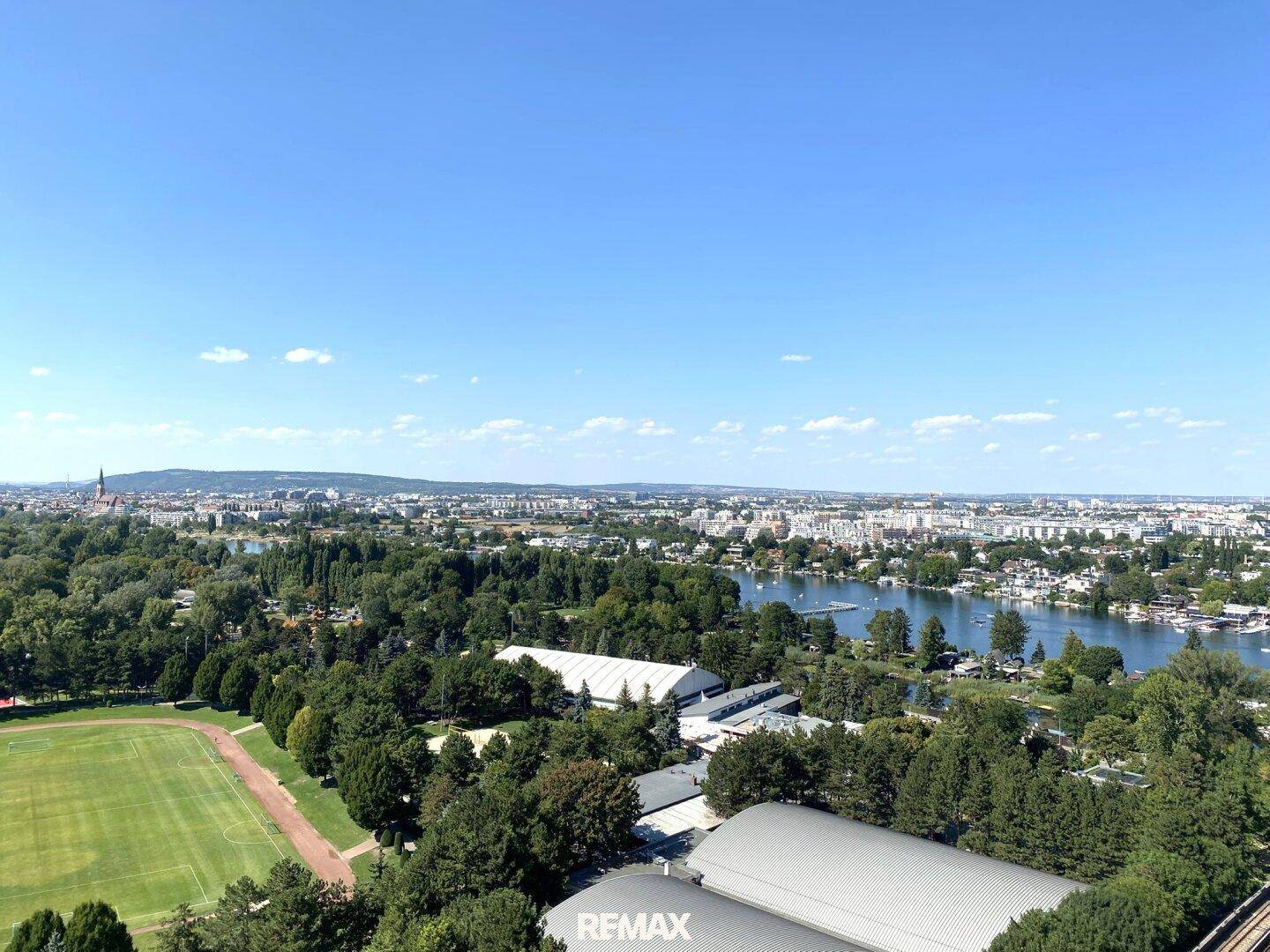 Weitläufiger Ausblick auf die Stadt, umgeben von viel Grün und einem See mit Uferbebauung.