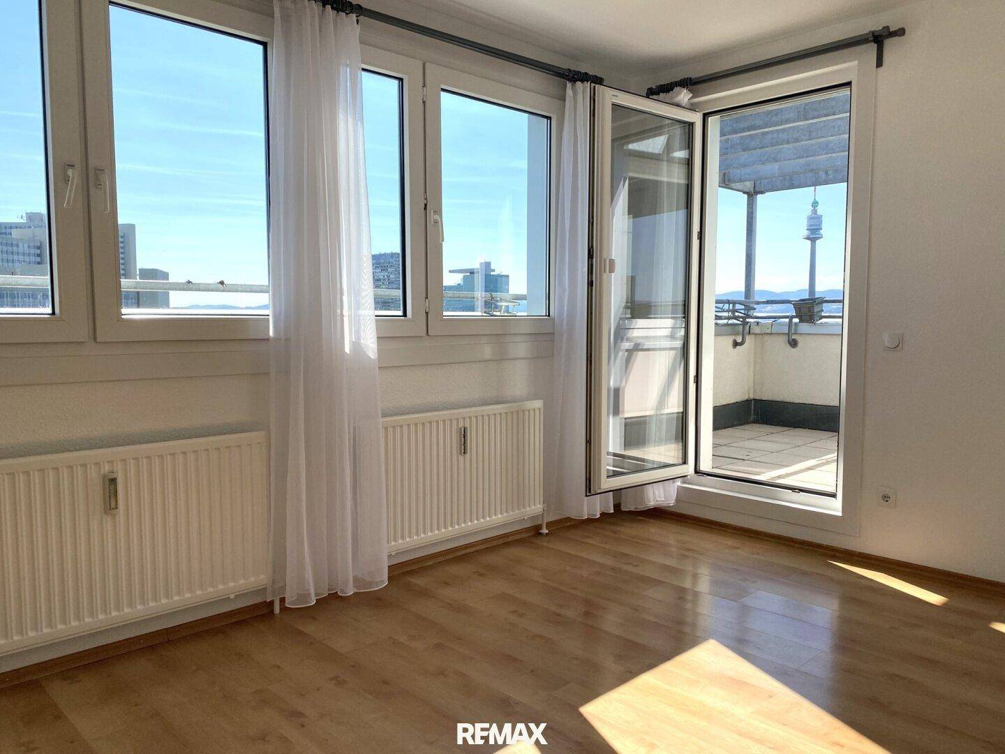 Helles Zimmer mit Holzboden, großen Fenstern und direktem Zugang zu einer sonnigen Terrasse.