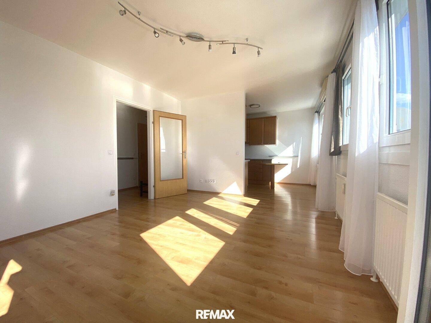 Heller Wohnbereich mit Holzboden und offener Verbindung zu einem weiteren Raum, ideal für flexibles Wohnen.