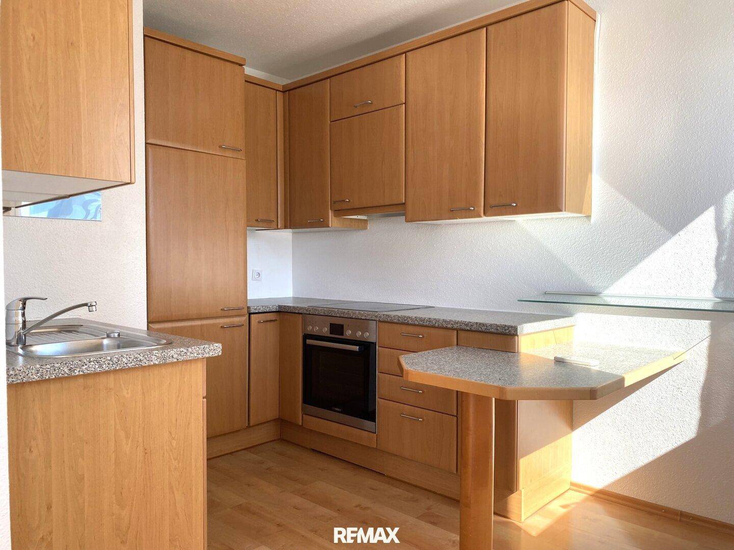 Funktionale Küche mit hellen Holzschränken, Granit-Arbeitsplatten und integriertem Backofen.