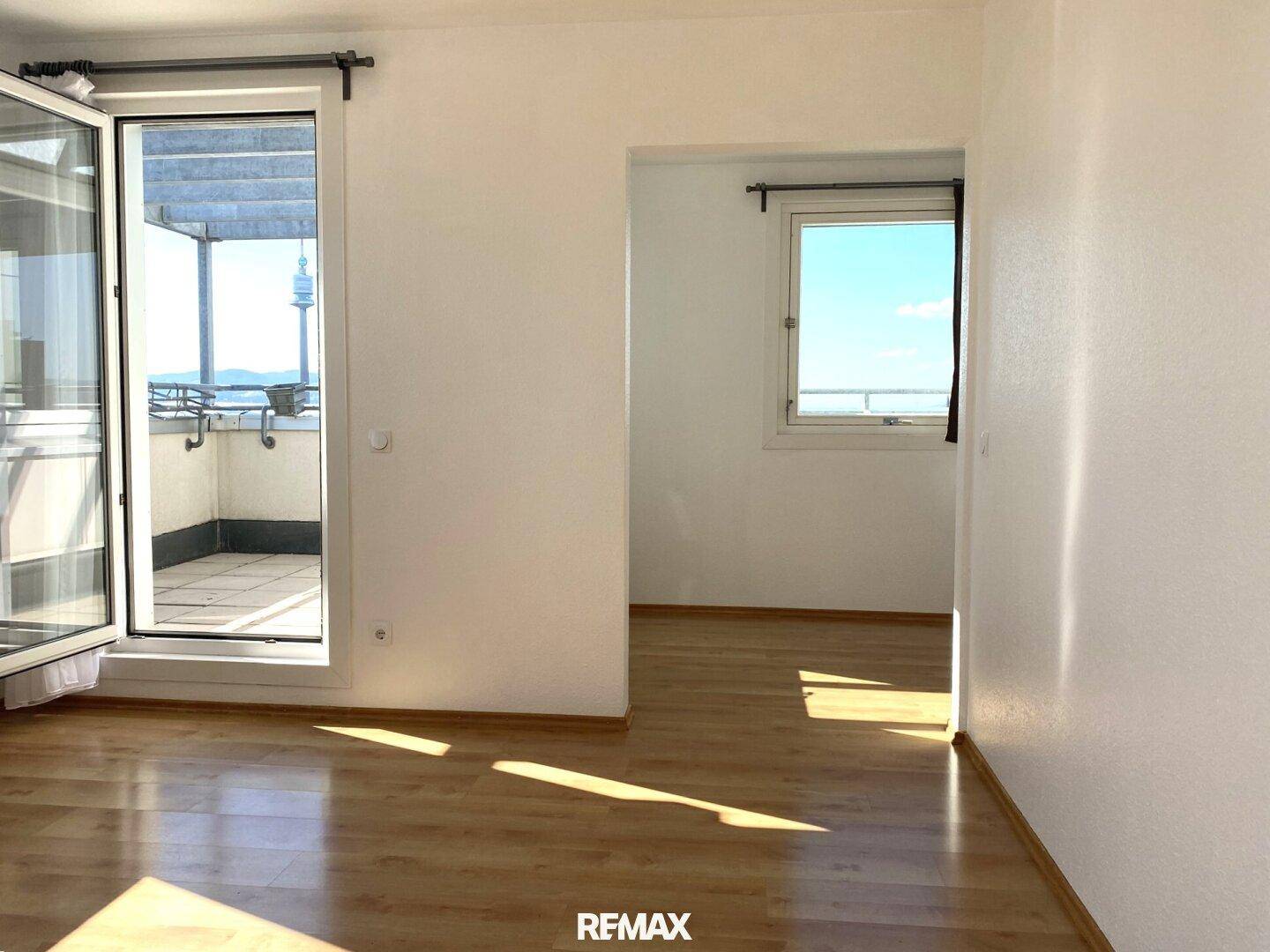 Leeres Zimmer mit Holzboden, großen Fenstern und direktem Zugang zur Außenterrasse.