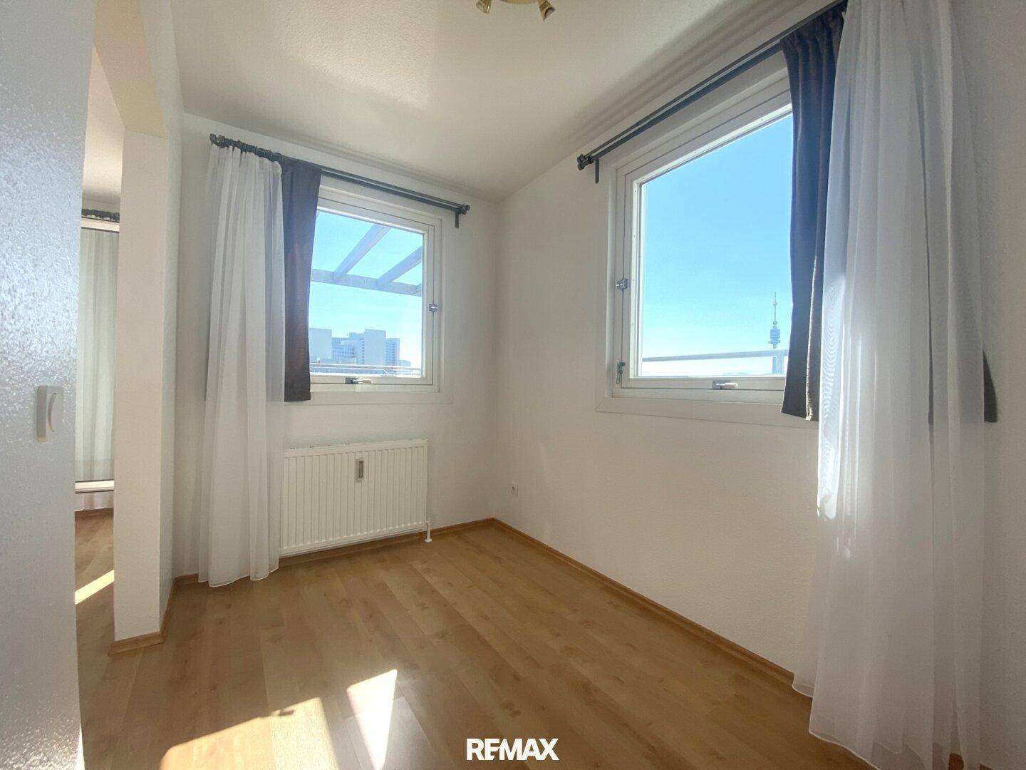 Helles Schlafzimmer mit Holzboden und zwei Fenstern, die viel Tageslicht hereinlassen.
