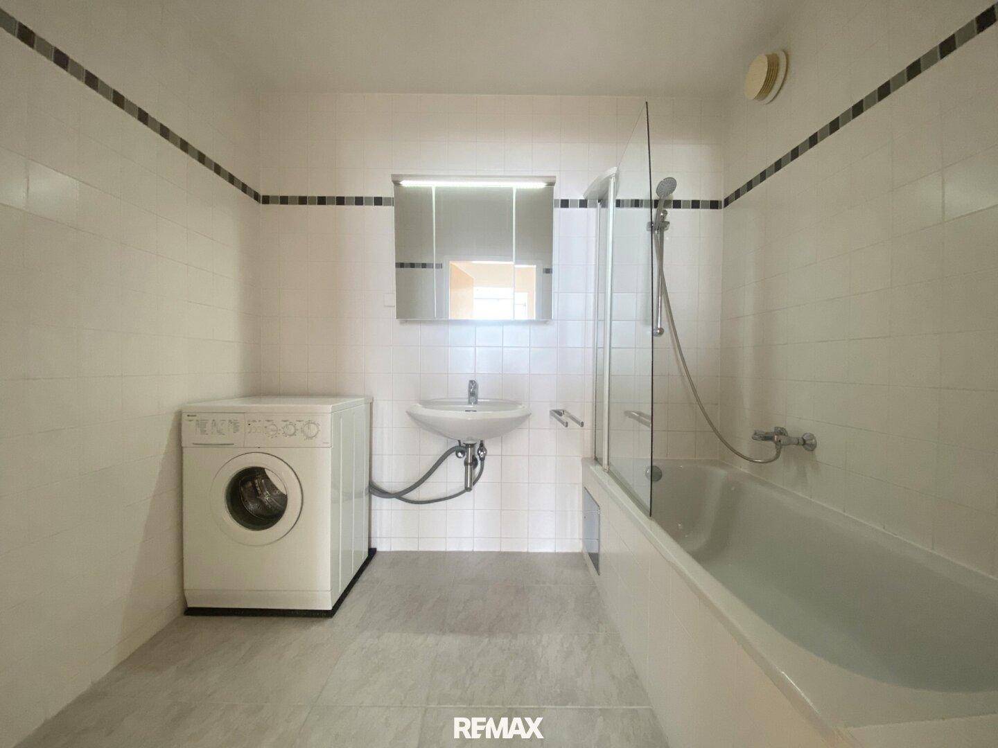 Gefliestes Badezimmer mit Badewanne, Duschfunktion, Waschbecken und Waschmaschine.