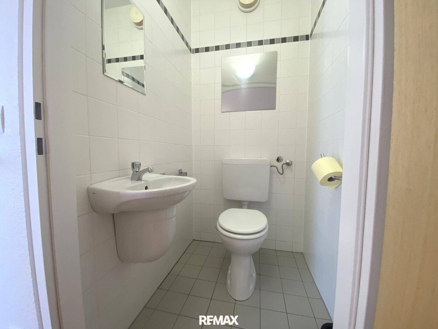 Separates Gäste-WC mit Fliesenboden, Toilette und kleinem Handwaschbecken.