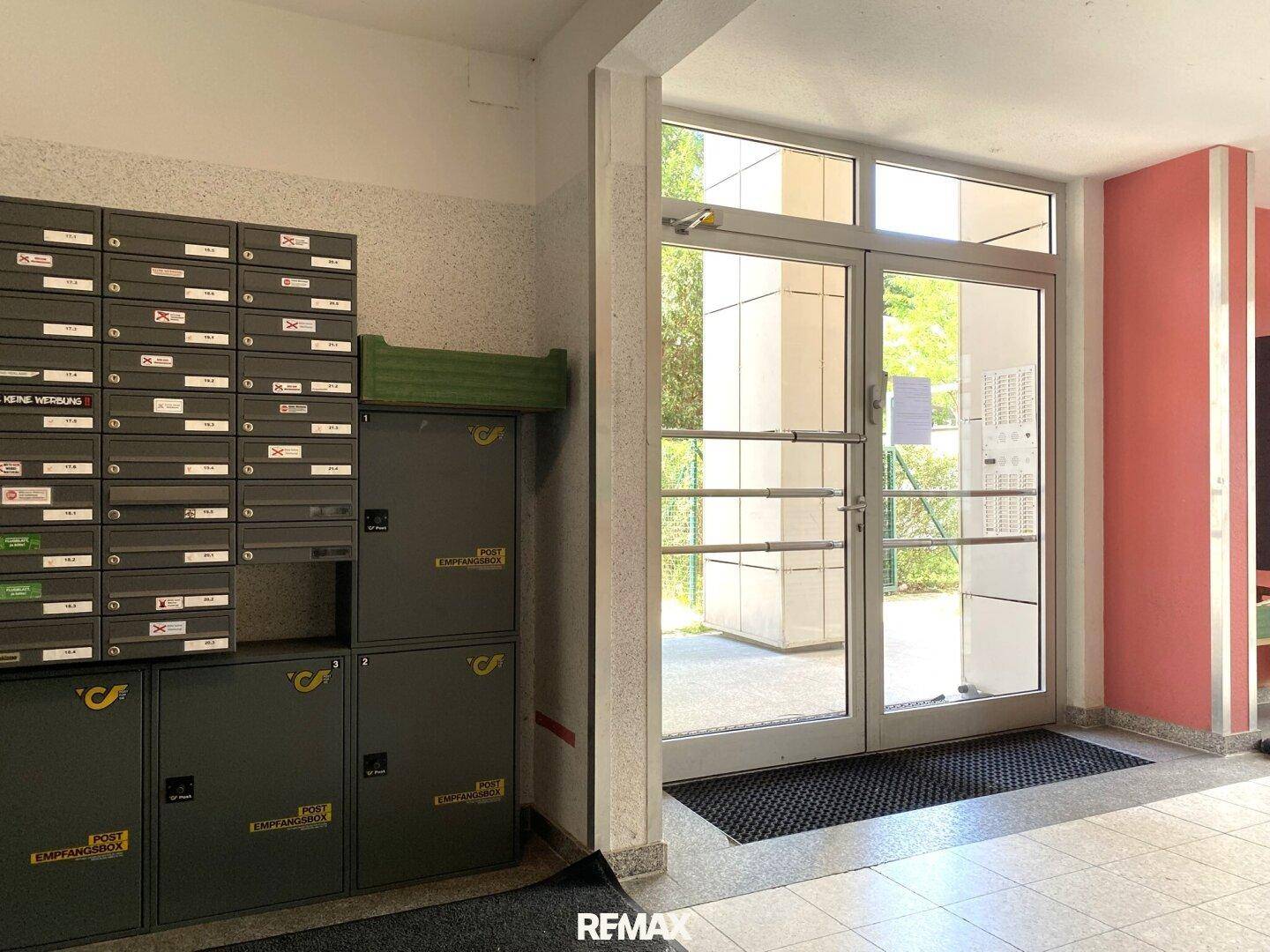 Eingangsbereich des Gebäudes mit Briefkästen und großen Glastüren zum Außenbereich.