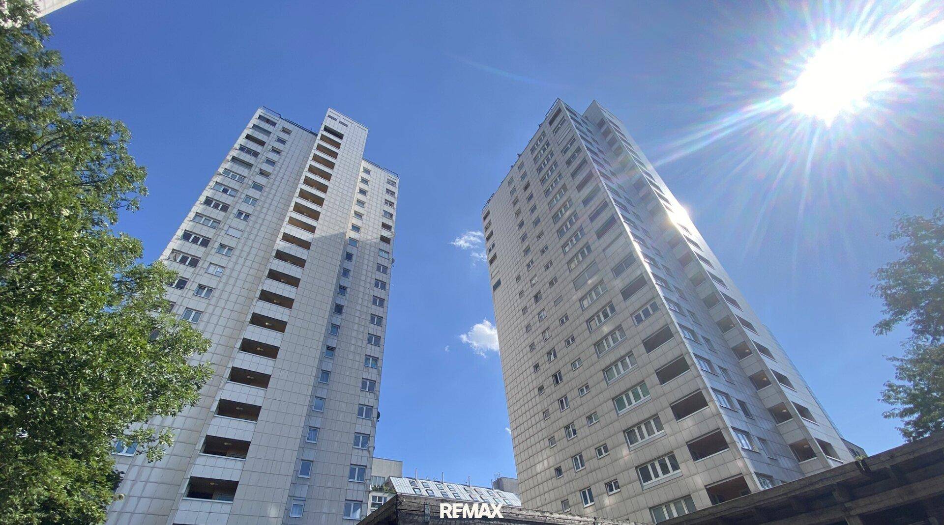 Zwei hohe Wohngebäude mit vielen Balkonen unter strahlend blauem Himmel.