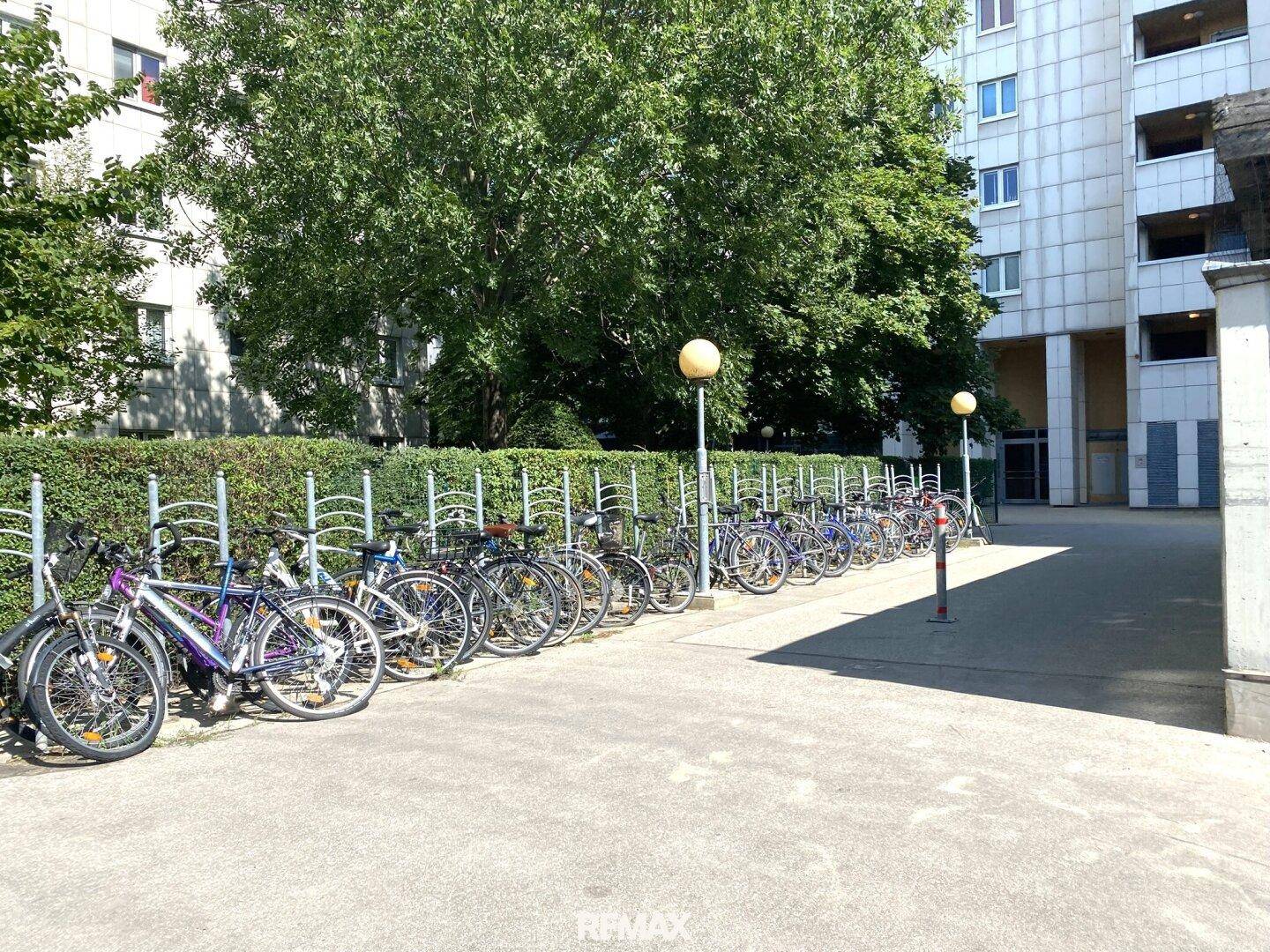 Fahrradabstellplätze im Freien vor dem Wohngebäude, umgeben von Grünflächen.