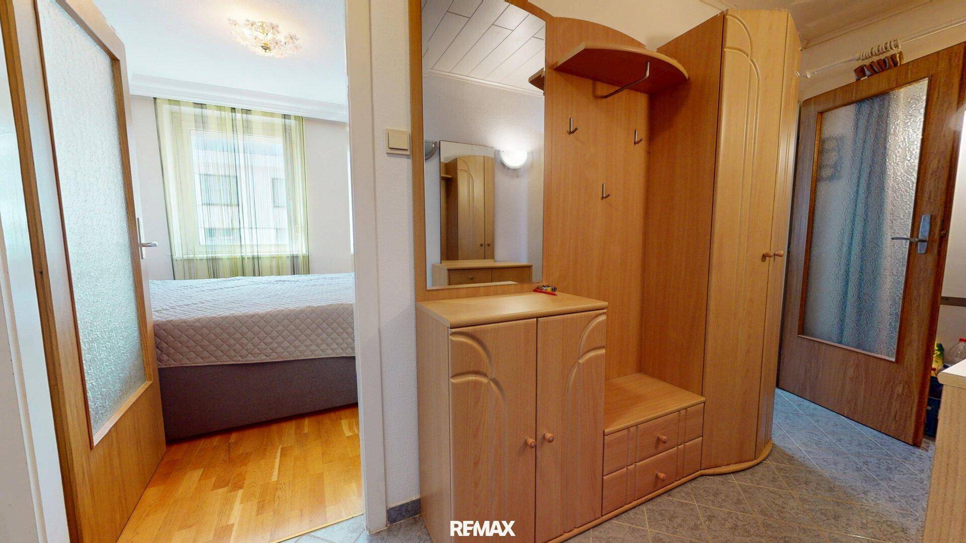 Eingangsbereich mit Garderobe, Spiegel und Fliesenboden, führt zum Schlafzimmer.
