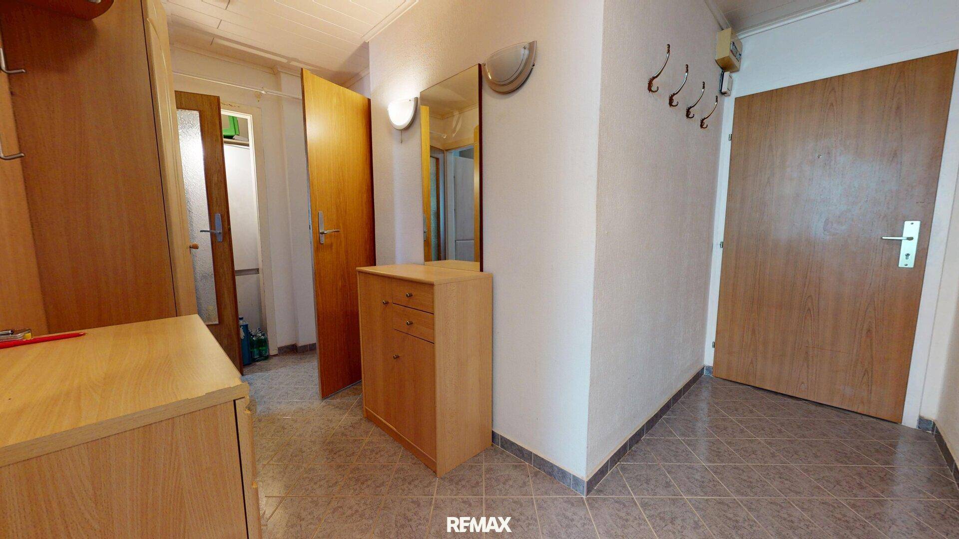 Flur mit Fliesenboden, Spiegel und Garderobe, bietet Zugang zu verschiedenen Räumen.