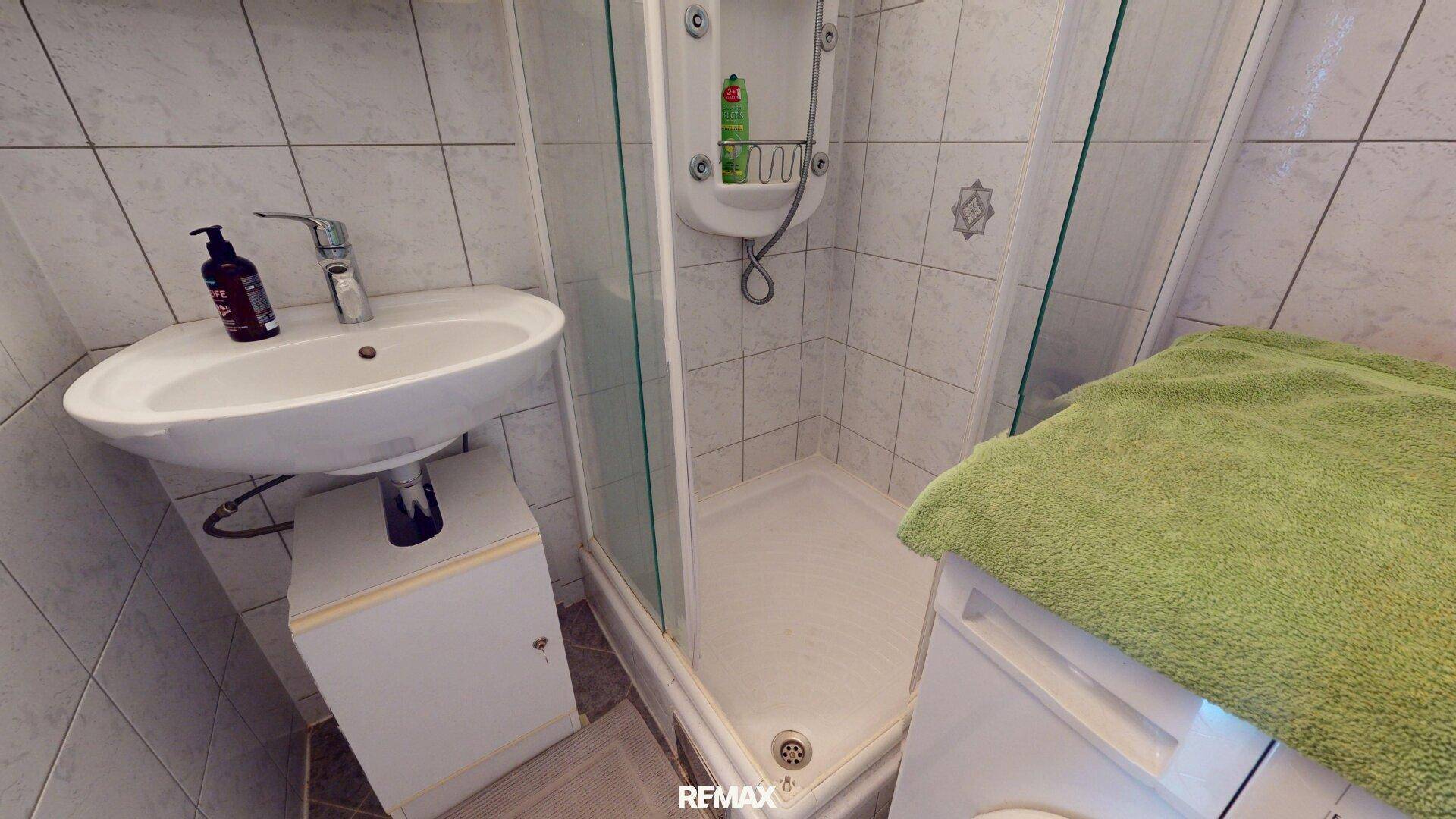 Badezimmer mit Waschbecken, Duschkabine und Fliesen an Wänden und Boden.