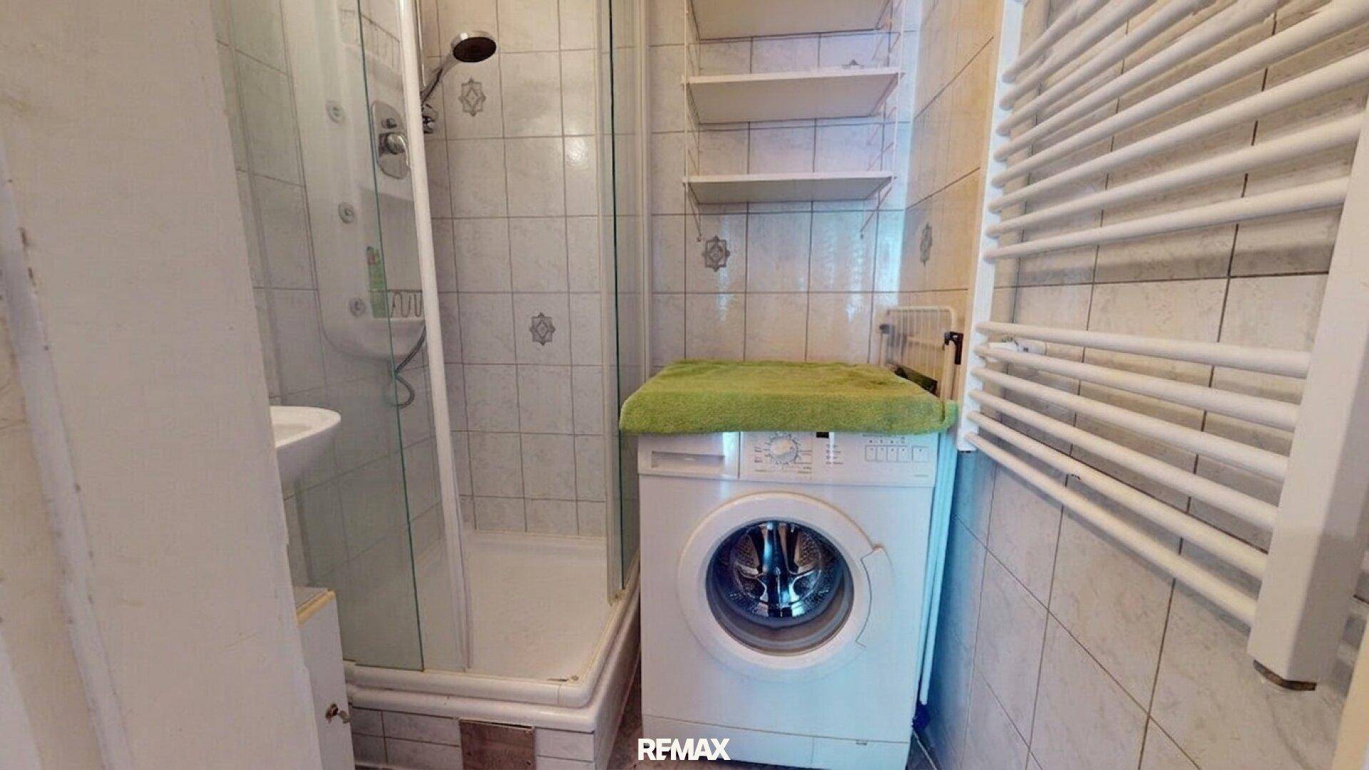 Badezimmer mit Dusche, Waschmaschine und Handtuchheizkörper, komplett gefliest.