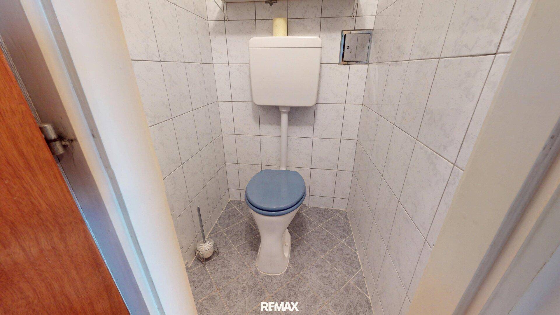 Separate Toilette mit WC und Fliesen an Wänden und Boden.