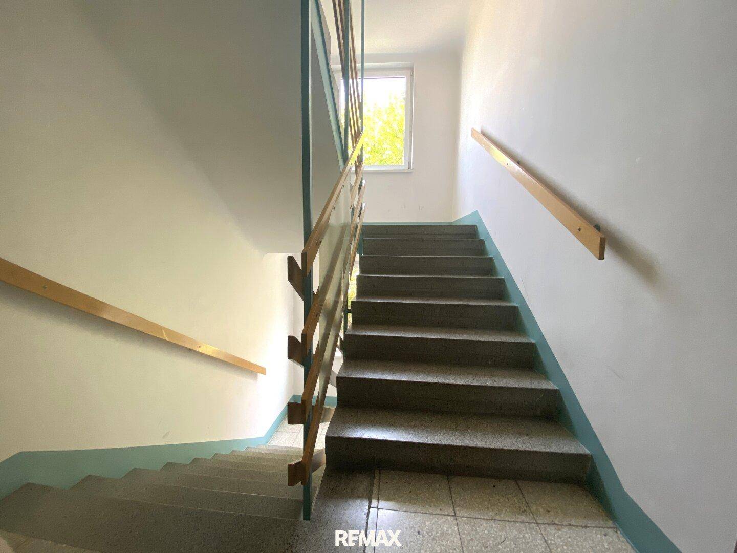 Treppenhaus mit Betonstufen und Holzgeländer, führt zu den oberen Etagen.