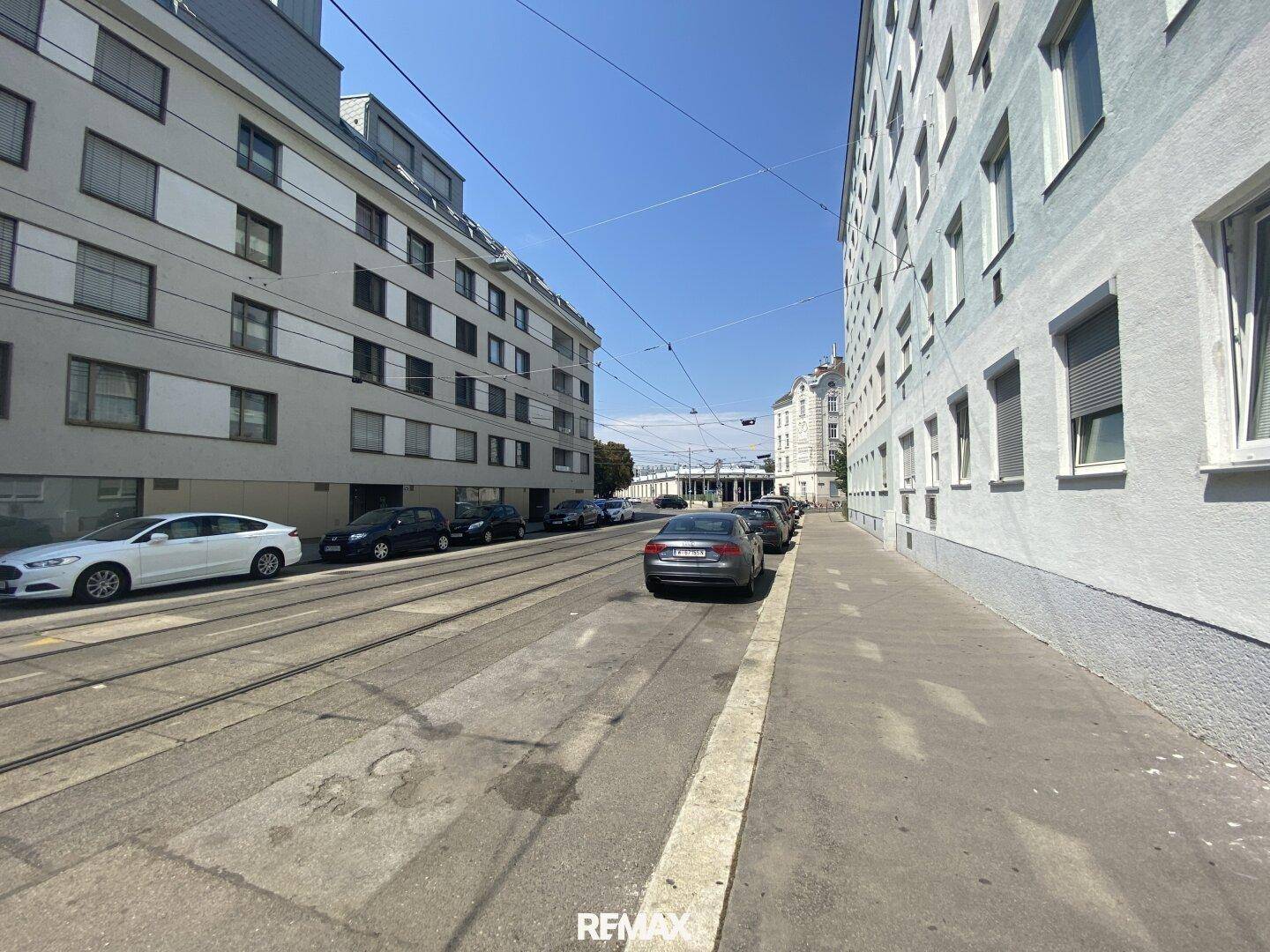 Stadtstraße mit parkenden Autos und Gebäuden unter blauem Himmel.