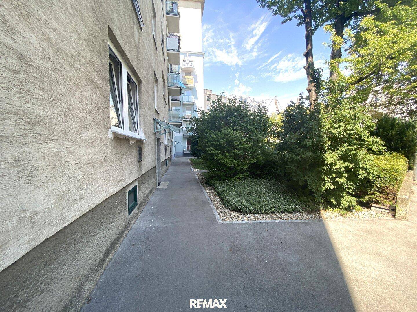 Gepflegter Gartenbereich neben dem Gebäude mit Sträuchern und Gehwegen.