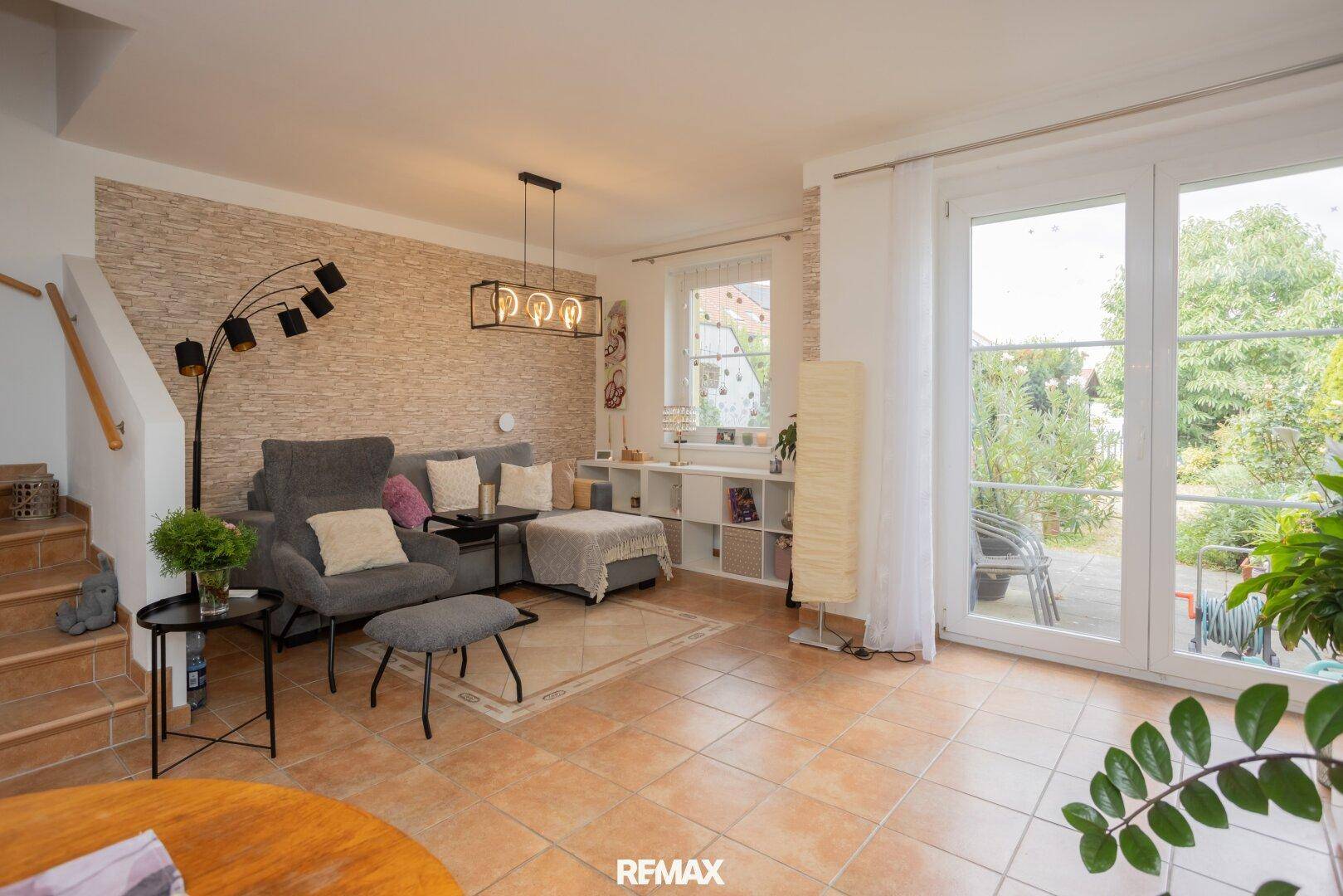 Helles Wohnzimmer mit beigem Fliesenboden, bequemer Couch und großem Fenster zum Garten.