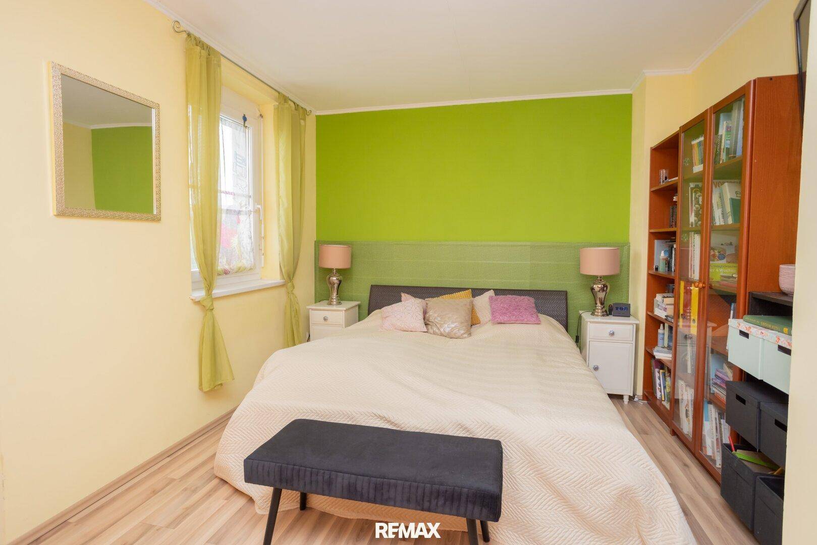Gemütliches Schlafzimmer mit Doppelbett, grüner Akzentwand und Laminatboden.