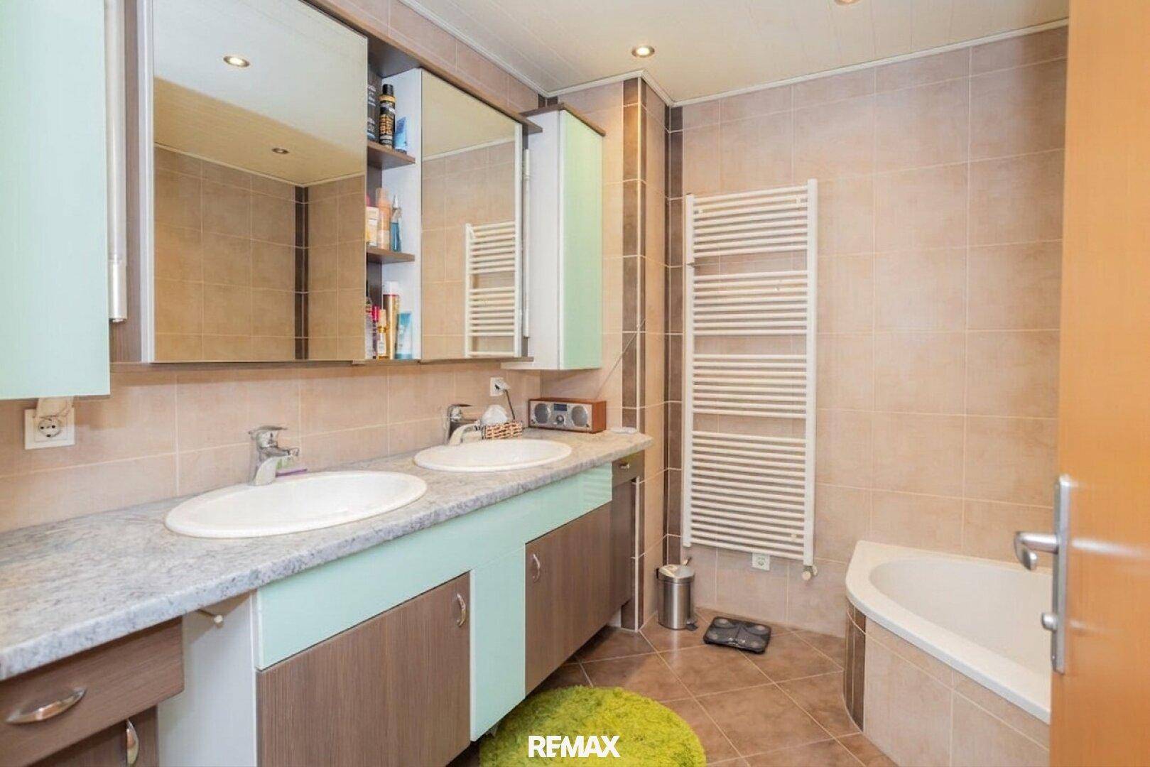 Badezimmer mit Doppelwaschbecken, beheiztem Handtuchhalter und einer Eckbadewanne.