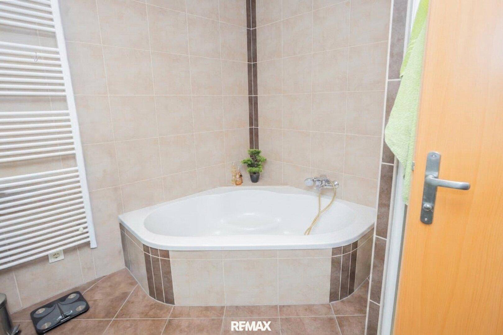 Nahaufnahme der Eckbadewanne im Badezimmer mit beigen Fliesen und Heizkörper.