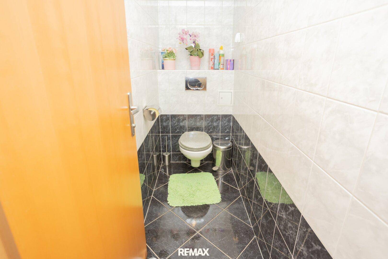 Gäste-WC mit wandhängender Toilette, dunklem Fliesenboden und hellen Wandfliesen.