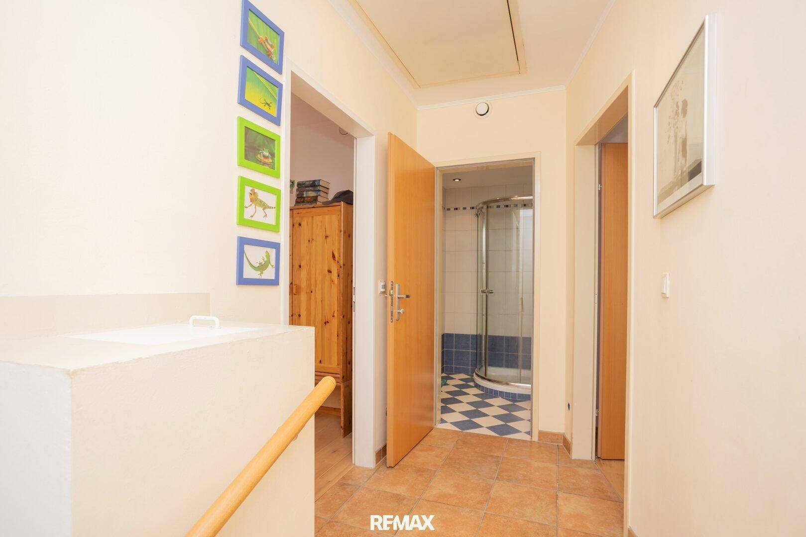 Flur mit Fliesenboden, der zu einem Badezimmer mit Duschkabine führt.