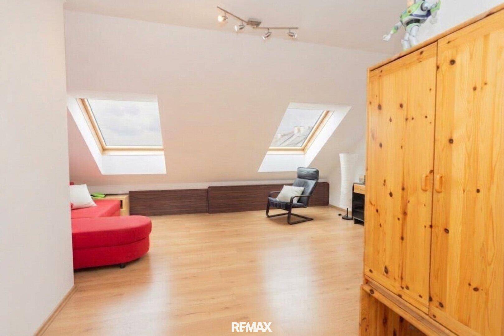 Helles Dachzimmer mit schrägen Decken, Dachfenstern und Laminatboden, möbliert.