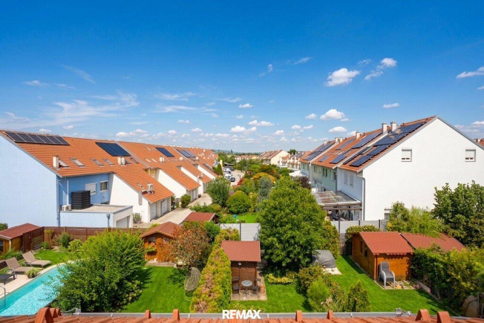 Luftaufnahme einer Wohnsiedlung mit Reihenhäusern, Gärten, Pool und Solaranlagen auf den Dächern.