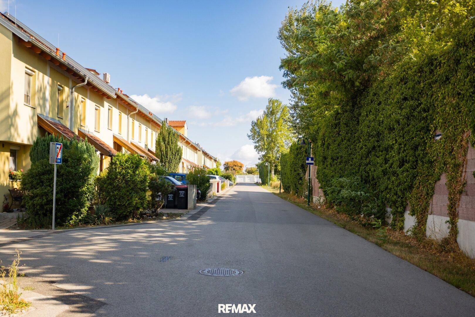 Ruhige Wohnstraße mit Reihenhäusern und einer begrünten Wand auf der gegenüberliegenden Seite.