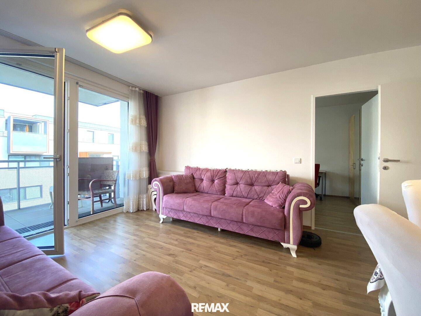 Geräumiges Wohnzimmer mit Holzboden und direktem Zugang zum Balkon.