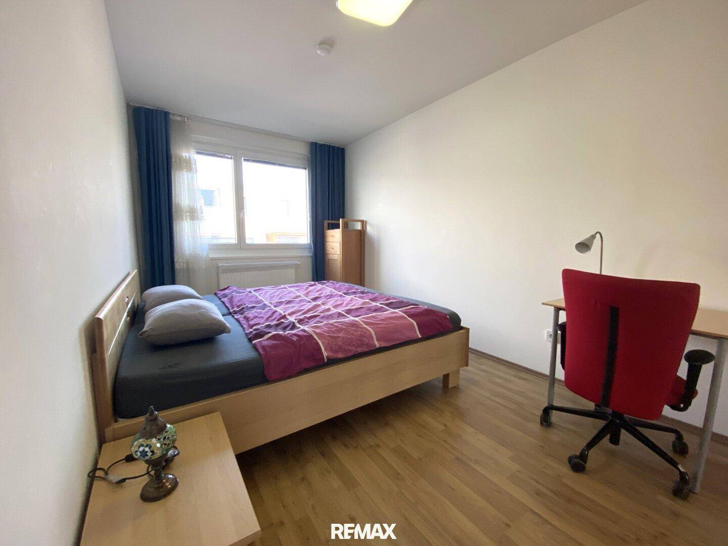 Schlafzimmer mit Holzboden, großem Fenster und Schreibtisch.