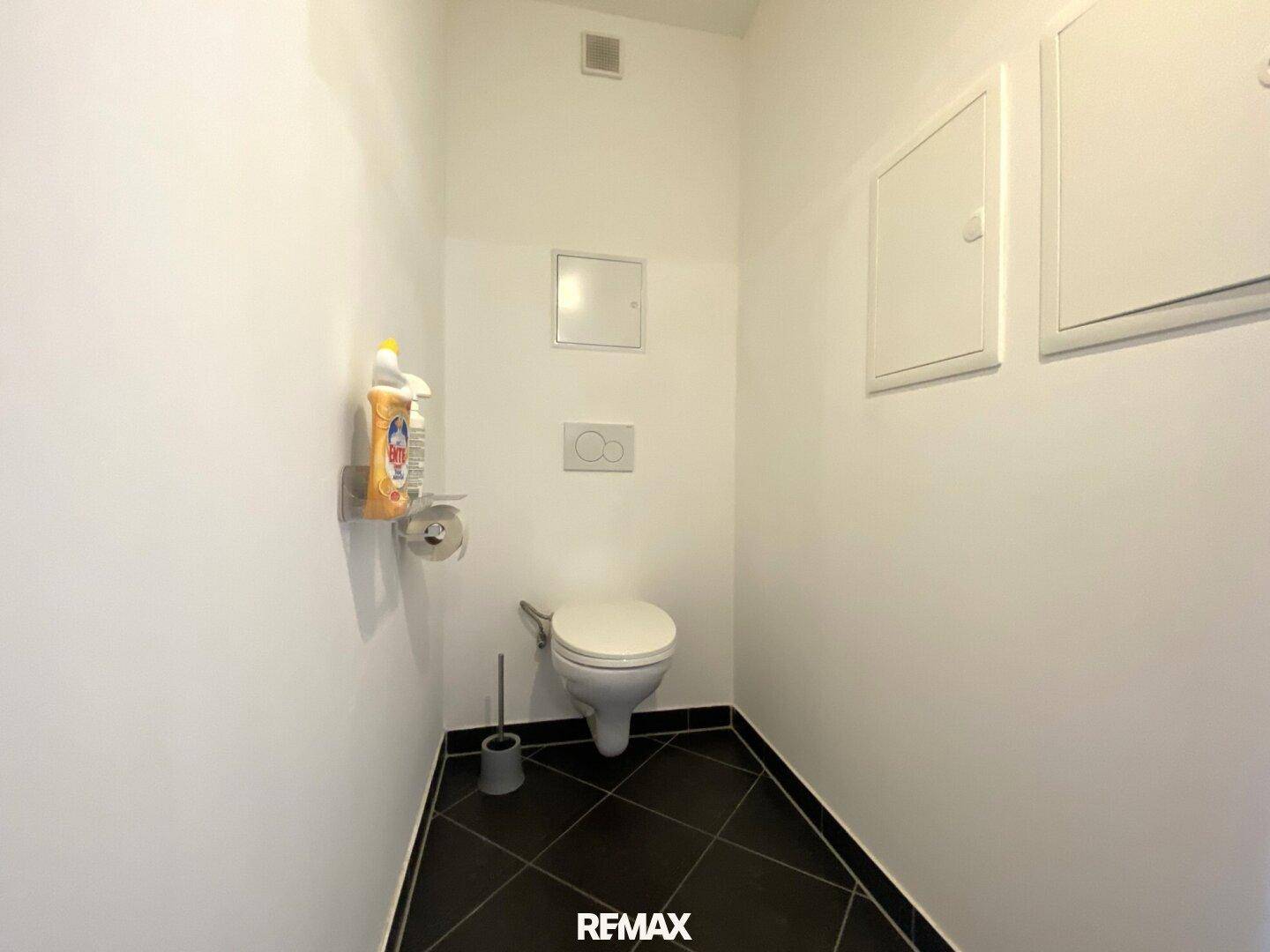 Separate Toilette mit Wand-WC und dunklen Fliesen.