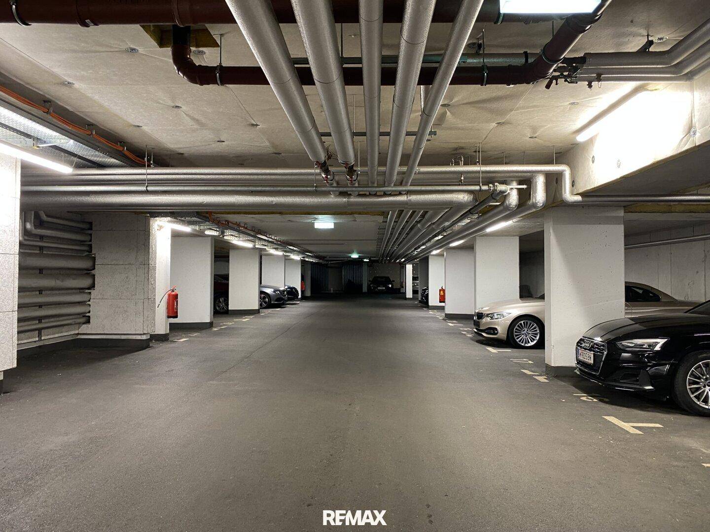 Tiefgarage mit mehreren Stellplätzen und sichtbaren Versorgungsleitungen.