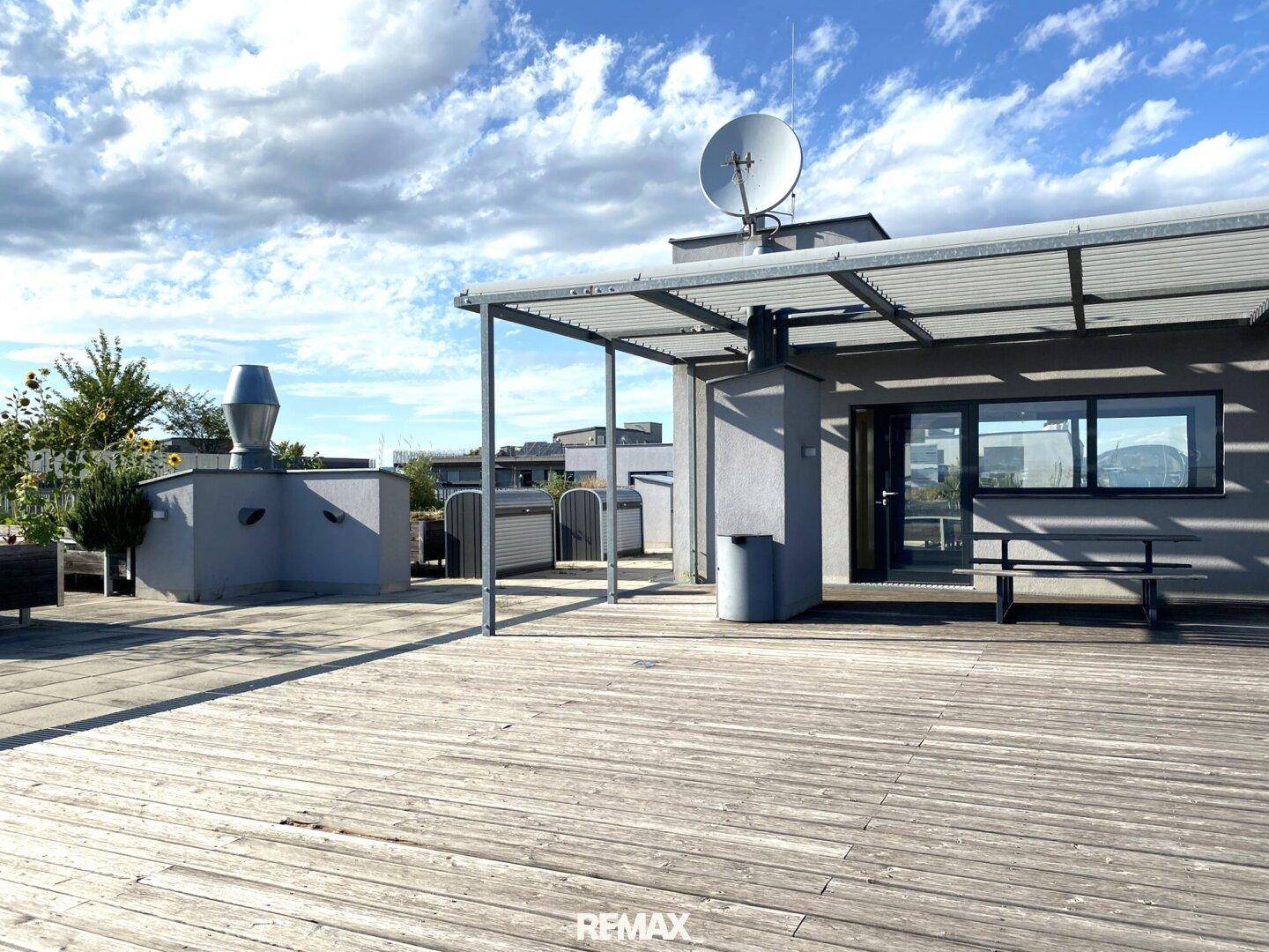 Große Dachterrasse mit Holzbelag, Überdachung und Satellitenschüssel.