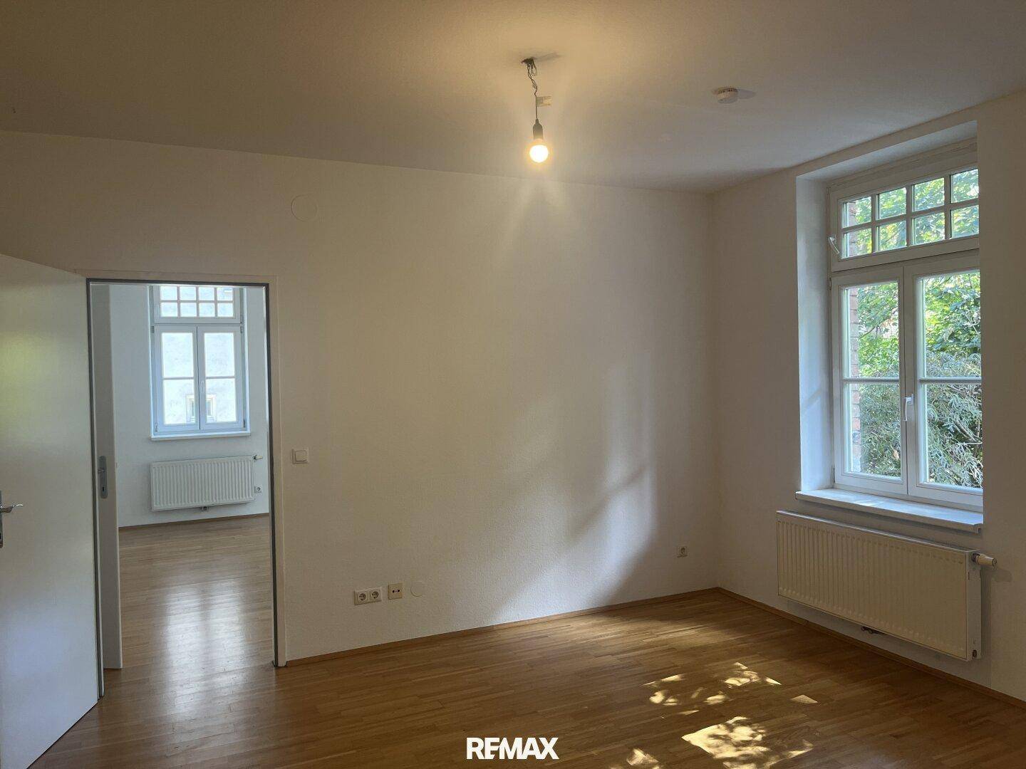 Geräumiges Wohnzimmer mit Parkettboden und großen Fenstern mit Blick ins Grüne.