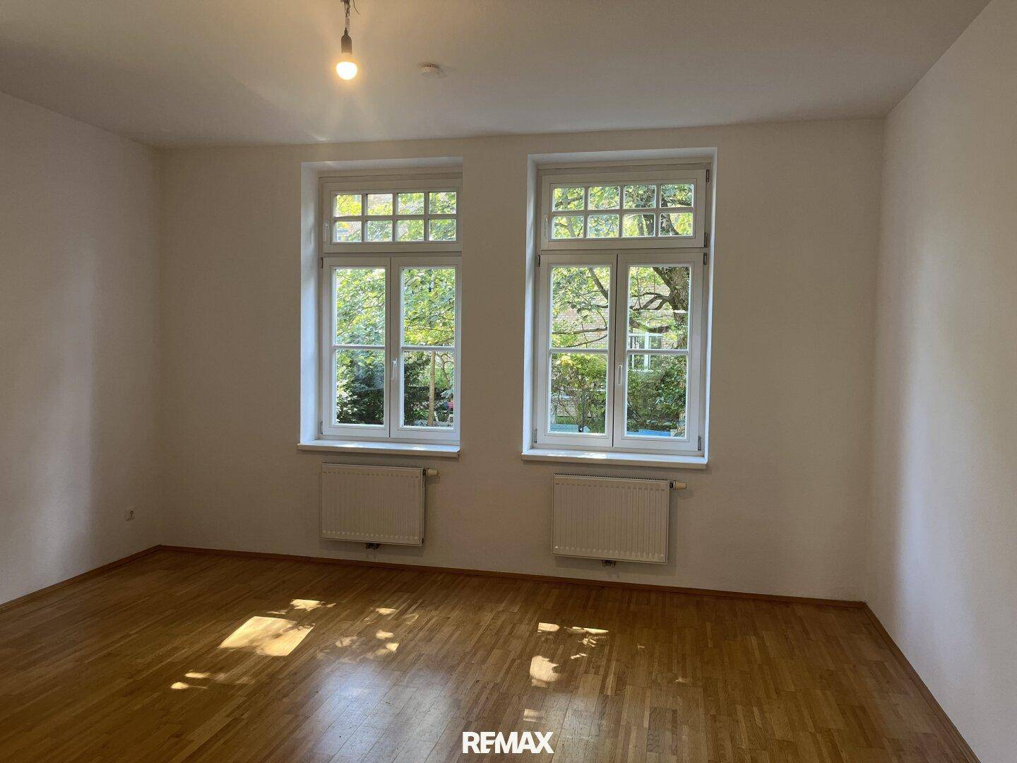 Helles Schlafzimmer mit zwei großen Fenstern und Blick auf die grüne Umgebung.