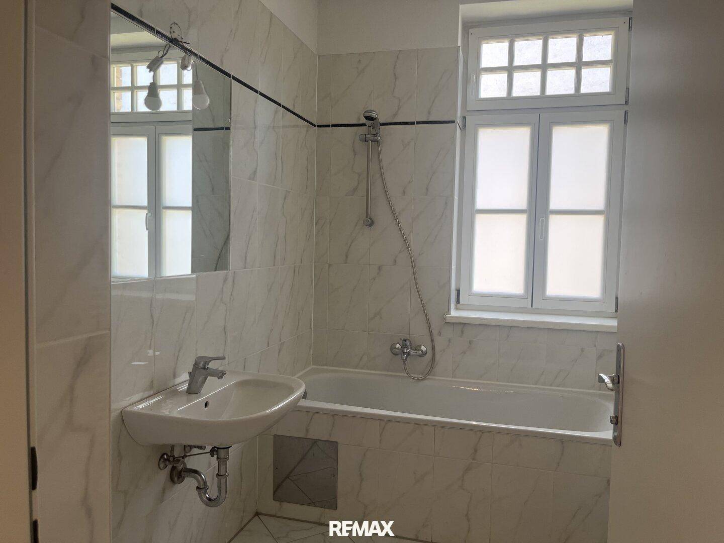 Modern gefliestes Badezimmer mit Badewanne, Waschbecken und Fenster.