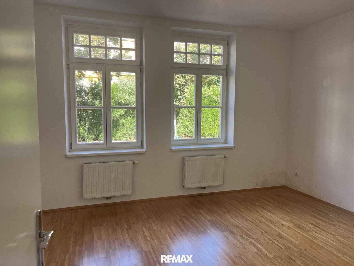 Geräumiges Schlafzimmer mit Parkettboden und zwei großen Fenstern.