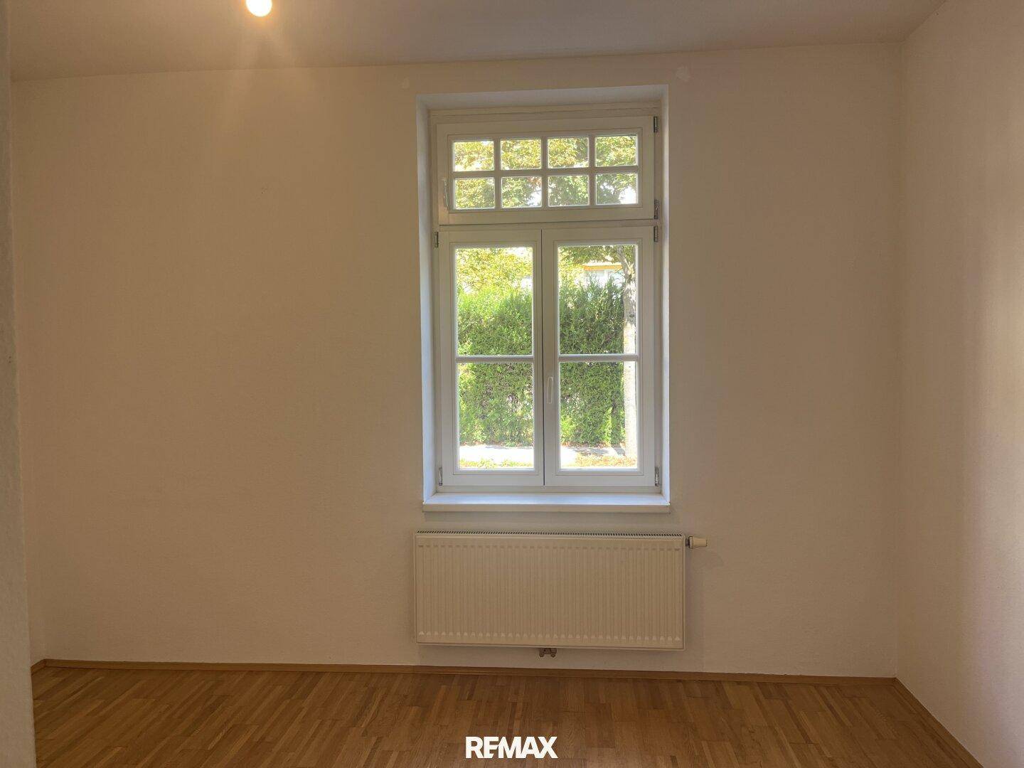 Helles Schlafzimmer mit Parkettboden und einem großen Fenster mit Blick ins Grüne.