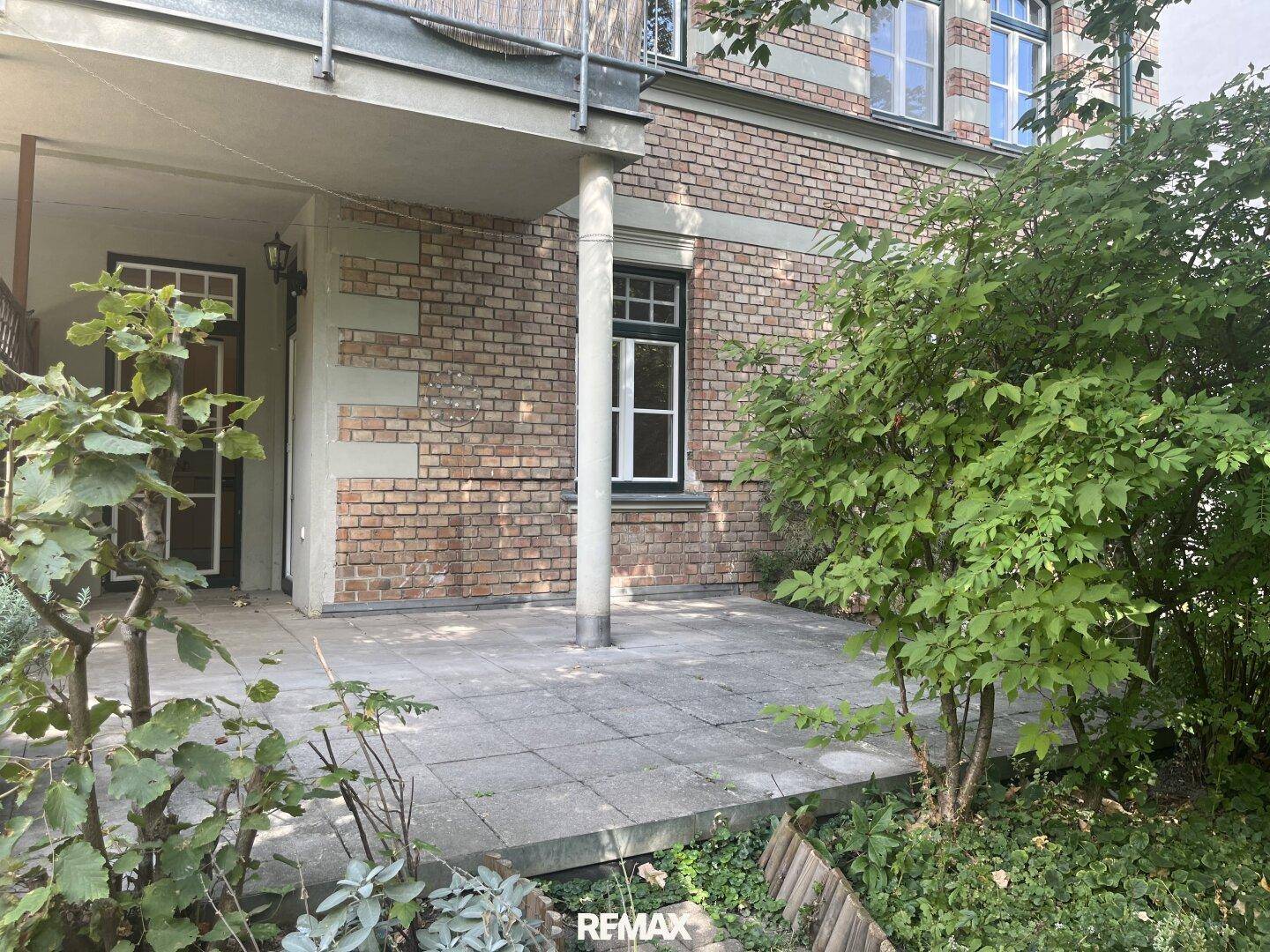 Überdachte Terrasse am Gebäude mit Ziegelmauerwerk und Zugang zum Garten.