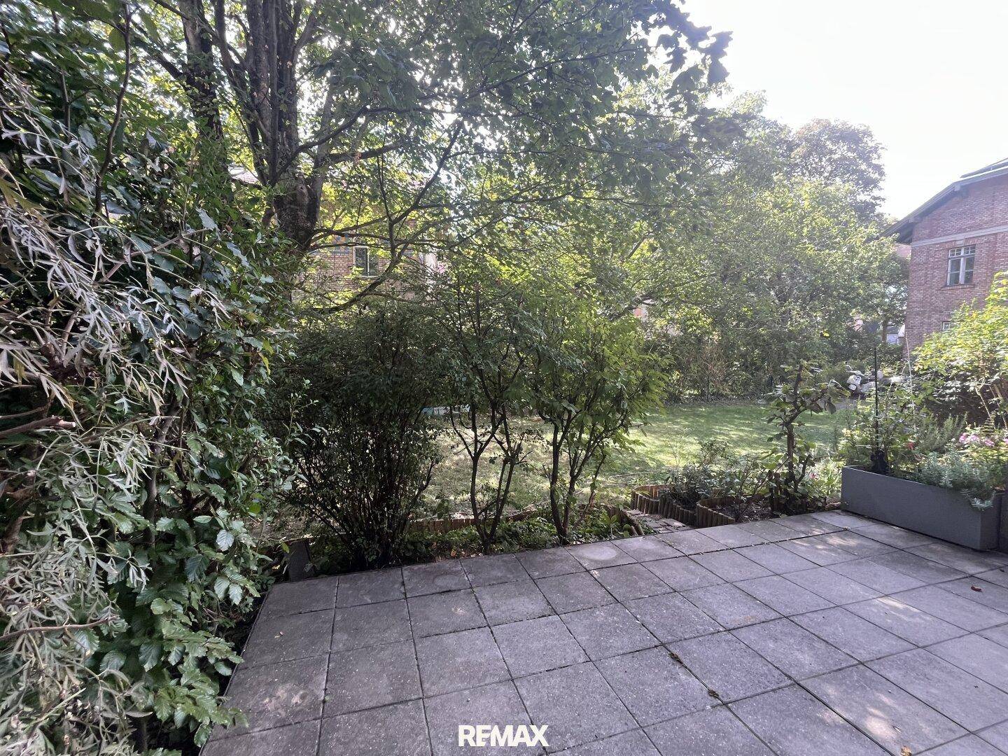 Sonniger Terrassenbereich mit Steinplatten und Blick auf den gepflegten Garten.
