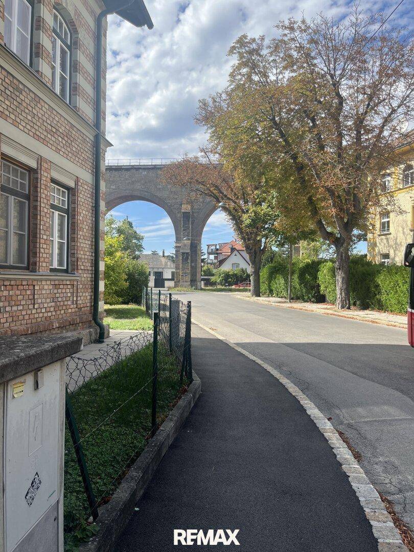 Blick auf eine historische Backsteinvilla an einer Straße mit einem alten Viadukt im Hintergrund.