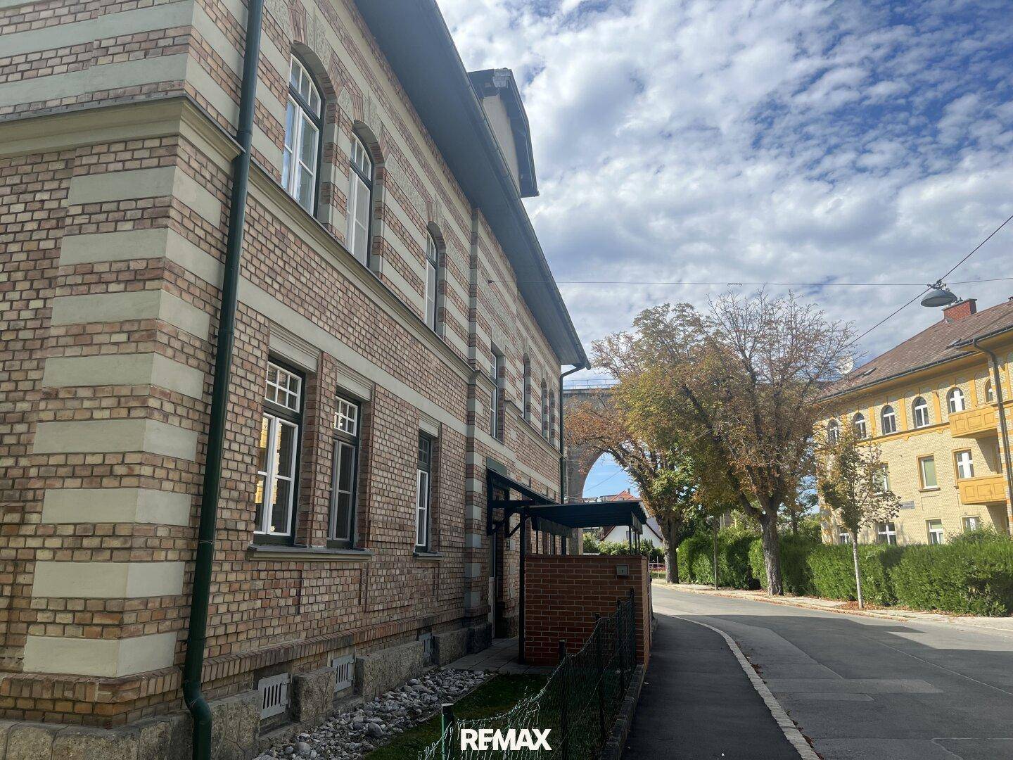 Seitenansicht einer charmanten Backsteinvilla mit markanten Fensterbögen und einem Viadukt in der Ferne.