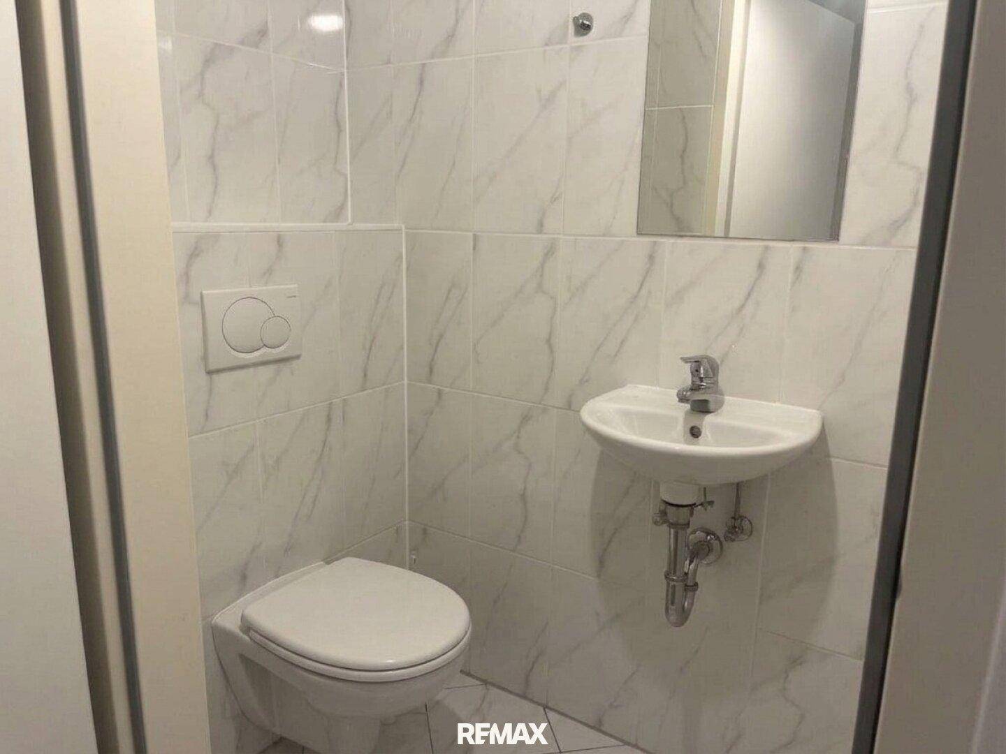 Separates WC mit Wand-WC, kleinem Waschbecken und modernen Fliesen.