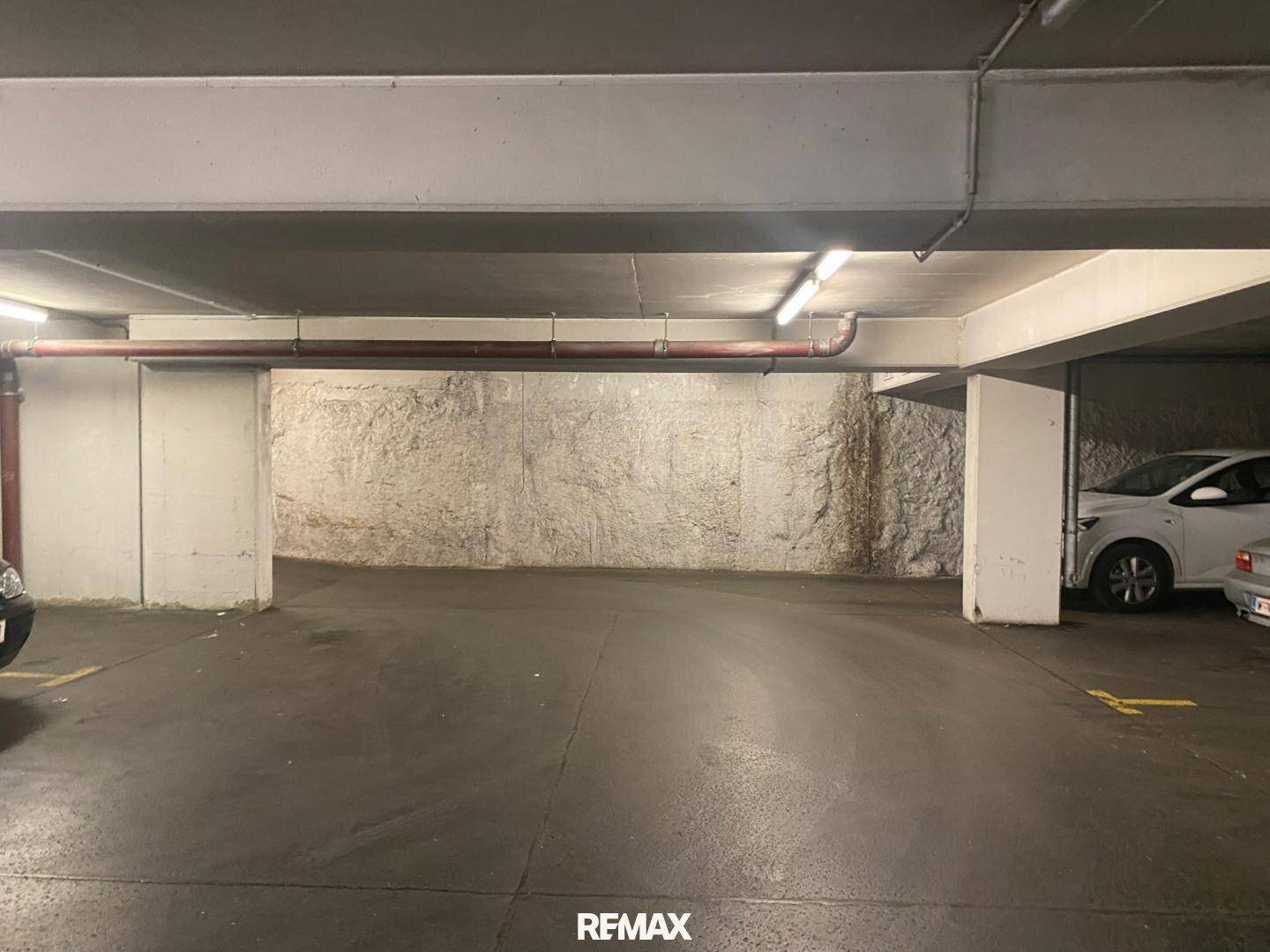 Geräumiger Bereich einer Tiefgarage mit Betonpfeilern und einer rauen Felswand im Hintergrund.
