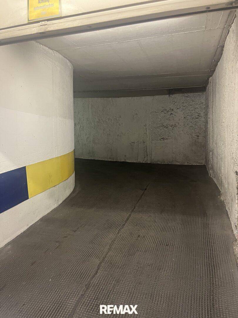 Gekrümmter Bereich einer Tiefgarage mit strukturierter Fahrbahn und farbigen Markierungen an der Wand.