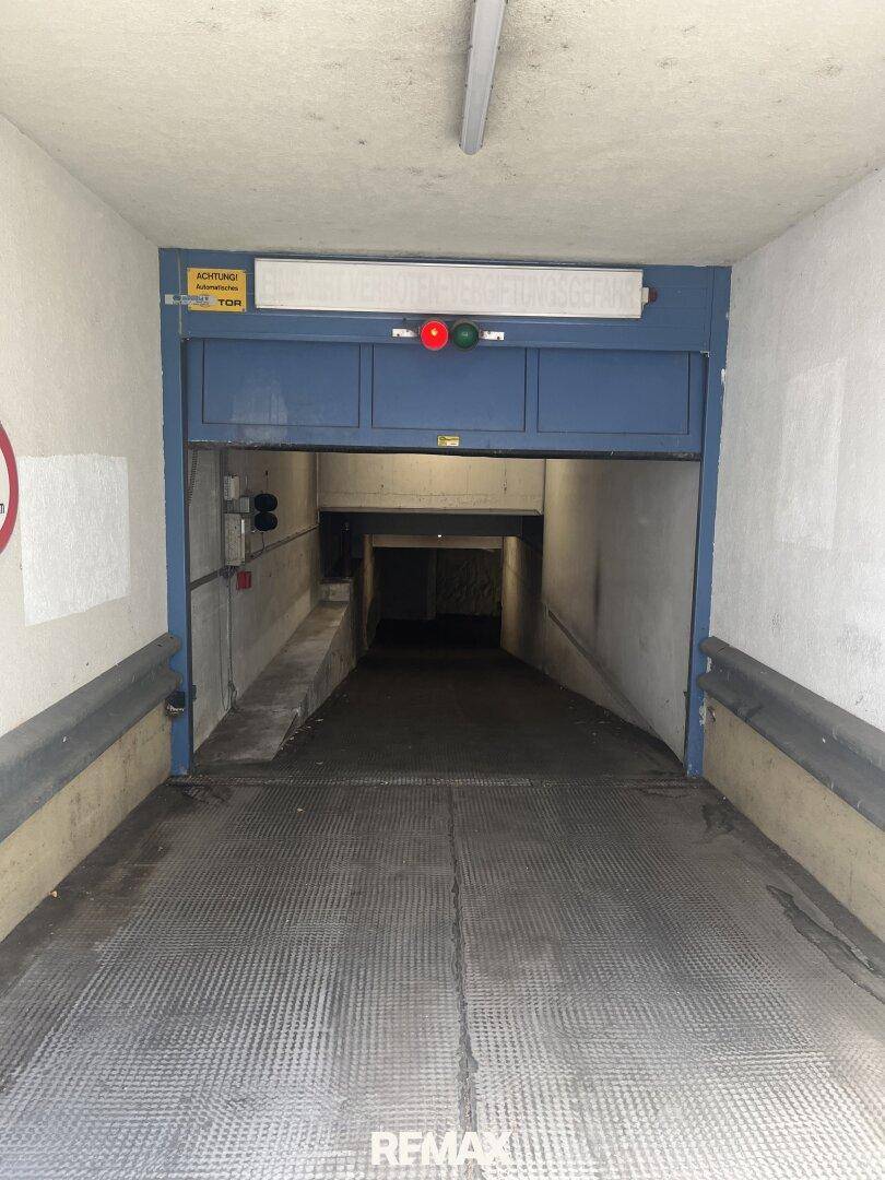 Einfahrt zu einer Tiefgarage mit blauer Schranke, Ampelsystem und strukturierter Rampe.